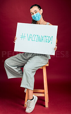 Mixed race covid vaccinated woman showing holding poster and wearing surgical face mask. Hispanic model isolated alone on red background in studio with copyspace. Promoting corona vaccine with sign