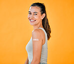 Mixed race covid vaccinated woman showing plaster on arm and smiling. Portrait of hispanic model isolated against yellow studio background with copyspace. Protected from corona with vaccine injection