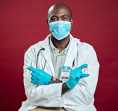 Buy stock photo African american covid doctor holding corona vaccine and needle while wearing surgical face mask. Portrait of black physician holding drug vial and syringe against red studio background with copyspace