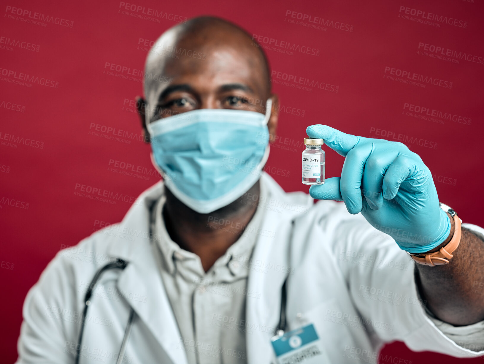 Buy stock photo African american covid doctor holding corona vaccine while wearing surgical face mask. Closeup portrait of black physician with drug vial against red studio background with copyspace. Virus protected