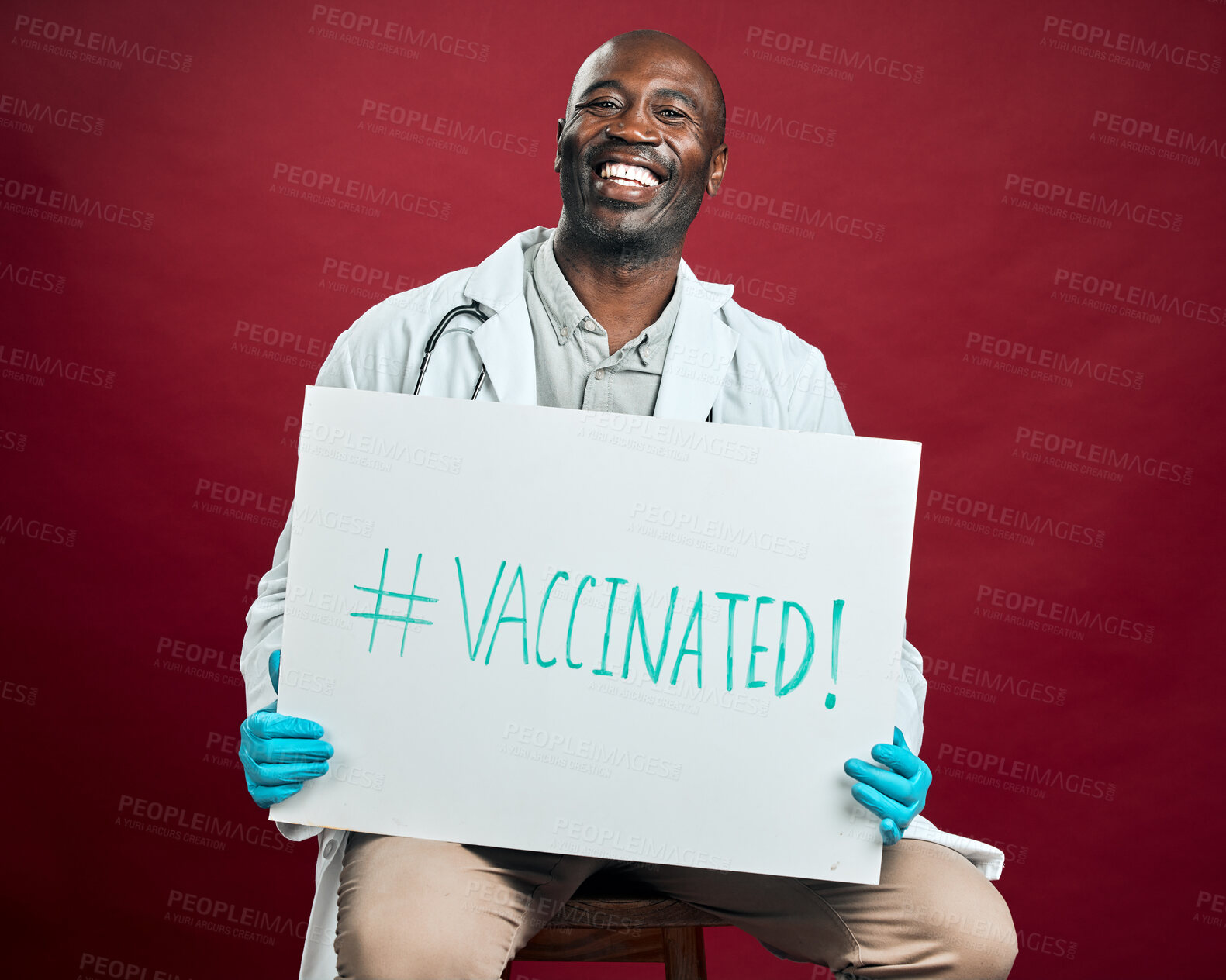 Buy stock photo African american covid doctor holding and showing poster. Portrait of smiling black physician isolated on red studio background with copyspace. Man promoting and encouraging corona vaccine on sign