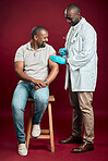 African american doctor giving covid vaccine to black man wearing surgical face mask. Full length healthy patient getting corona injection from physician against red studio background with copyspace