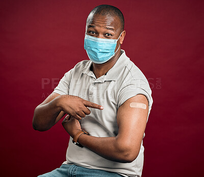 Buy stock photo African american covid vaccinated man pointing at arm plaster and wearing surgical face mask. Black model isolated on red studio background with copyspace. Using hand gesture, showing corona vaccine