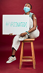 African american covid vaccinated woman showing arm plaster, holding poster, wearing surgical face mask. Happy black model isolated on red studio background with copyspace. Corona vaccine promote sign