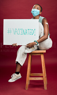 African american covid vaccinated woman showing arm plaster, holding poster, wearing surgical face mask. Happy black model isolated on red studio background with copyspace. Corona vaccine promote sign