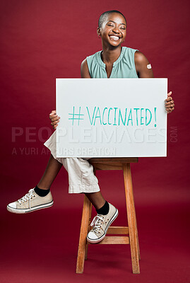 Buy stock photo African american covid vaccinated woman showing and holding poster. Full length of smiling black woman isolated against red studio background with copyspace. Model promoting corona vaccine with sign