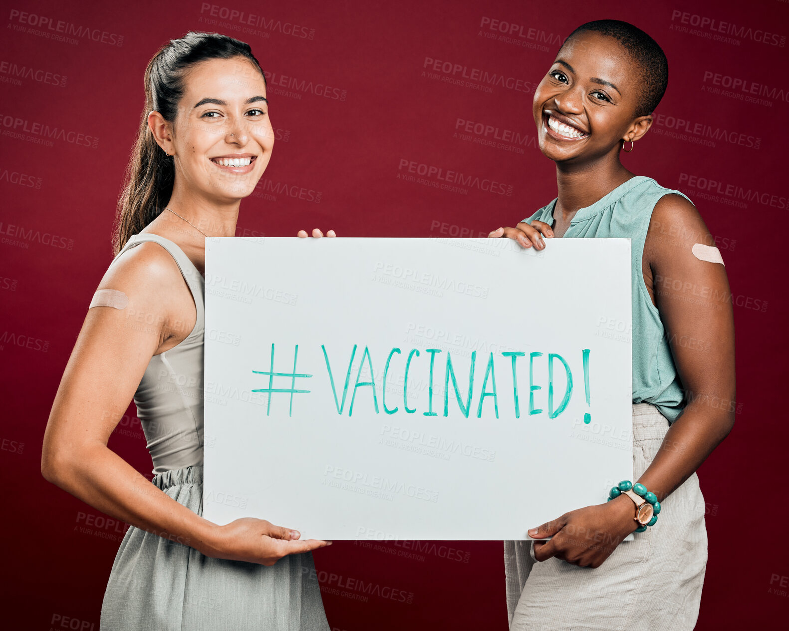 Buy stock photo Covid vaccinated African american and mixed race women showing and holding poster. Two people isolated on red studio background with copyspace. Showing plaster on arm and promoting corona vaccine