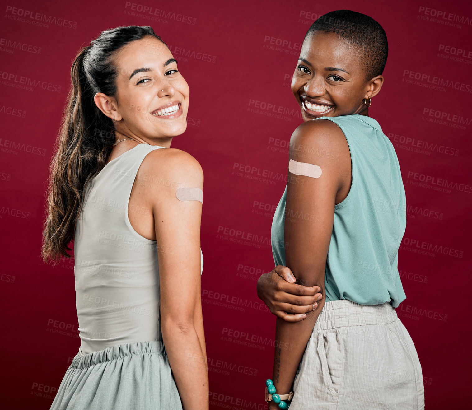 Buy stock photo Covid vaccinated African american and mixed race women showing arm plaster. Portrait of two happy people isolated on red studio background with copyspace. Black woman and hispanic with corona vaccine