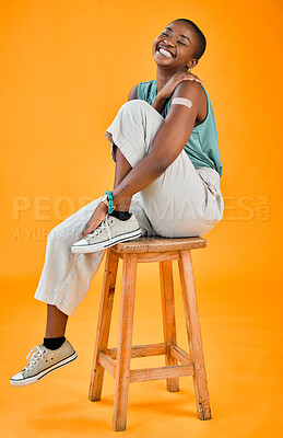 African american covid vaccinated woman showing plaster on arm and smiling. Full length black model isolated against yellow studio background with copyspace. Protected from corona in vaccine injection