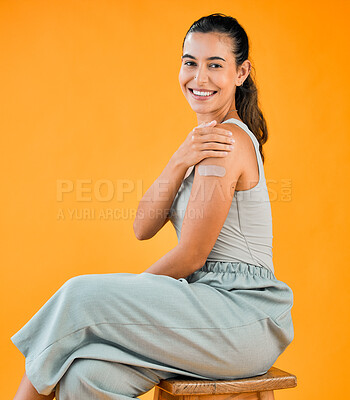 Buy stock photo Mixed race covid vaccinated woman showing plaster on arm and smiling. Portrait of hispanic model isolated against yellow studio background with copyspace. Protected from corona with vaccine injection