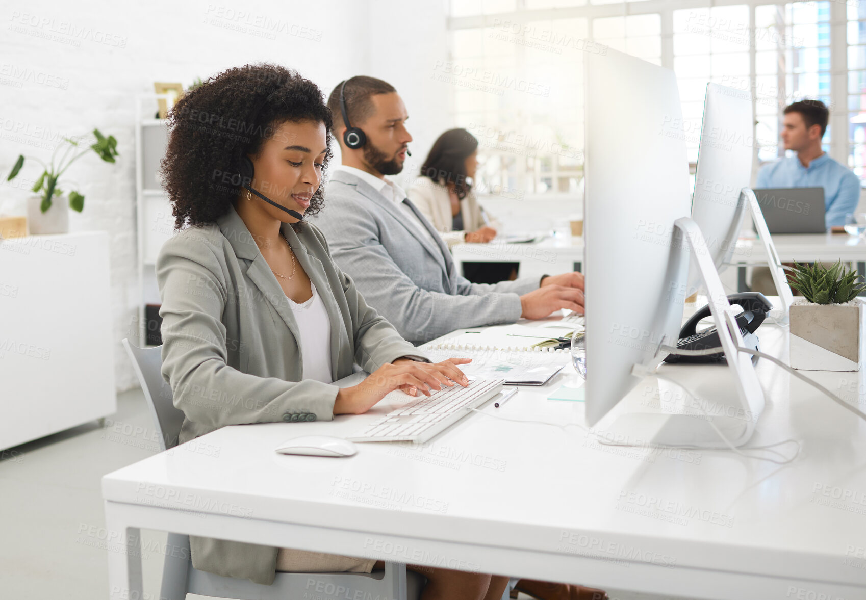 Buy stock photo Young happy mixed race female call center agent answering calls while wearing a headset at work. Hispanic businesswoman with a curly afro talking on a call while typing on a desktop computer at a desk in an office