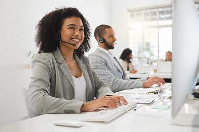 Young happy mixed race female call center agent answering calls while wearing a headset at work. Hispanic businesswoman with a curly afro talking on a call while using a desktop computer at a desk in an office