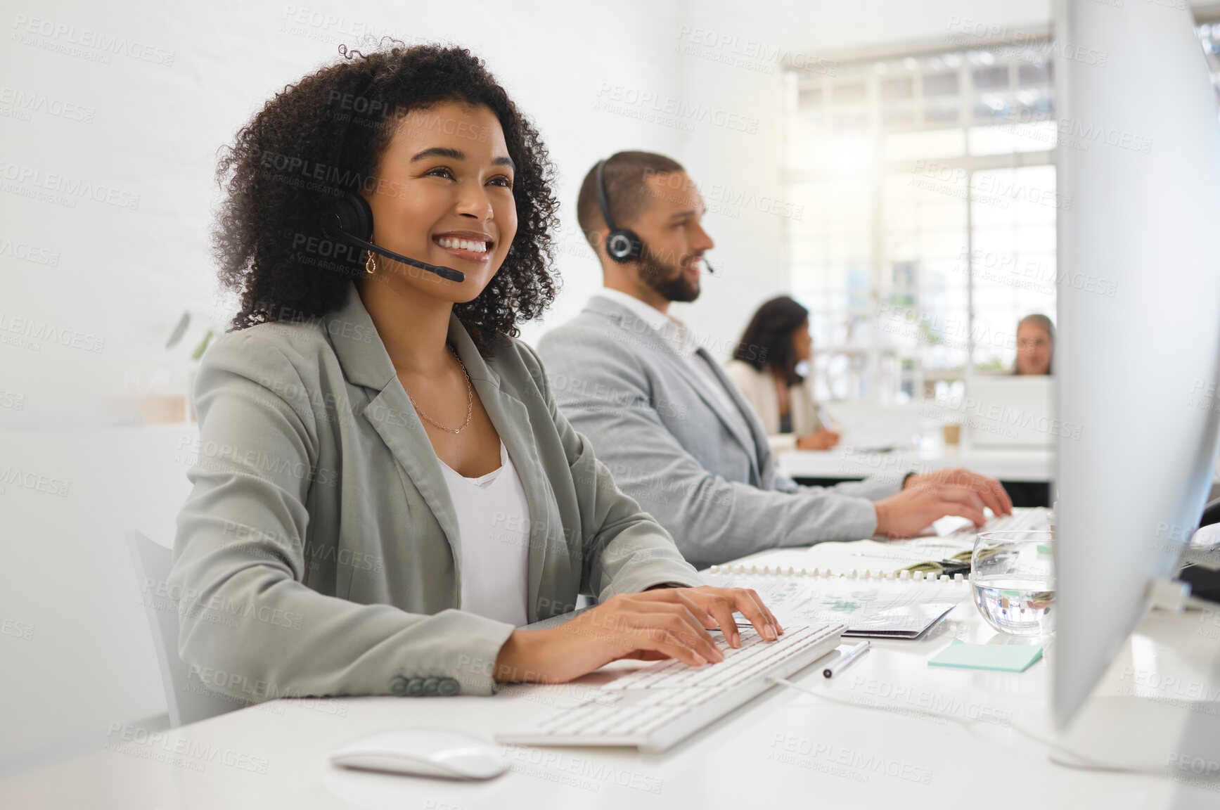Buy stock photo Young happy mixed race female call center agent answering calls while wearing a headset at work. Hispanic businesswoman with a curly afro talking on a call while using a desktop computer at a desk in an office
