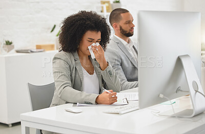 Young mixed race businesswoman blowing her nose with a tissue while sitting at a desk at work. Sick hispanic female businessperson with a curly afro writing on paper while suffering from allergies at work
