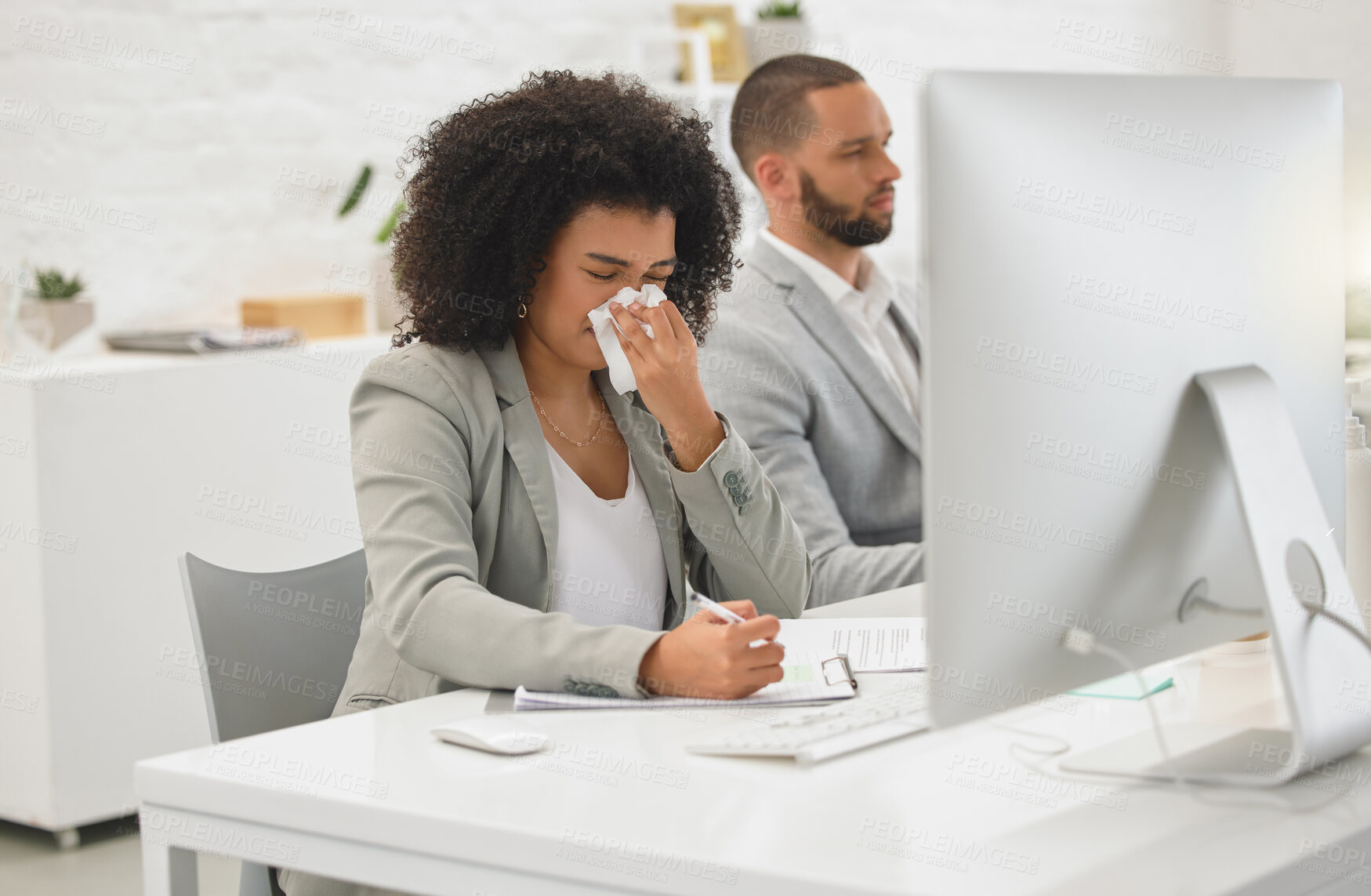 Buy stock photo Young mixed race businesswoman blowing her nose with a tissue while sitting at a desk at work. Sick hispanic female businessperson with a curly afro writing on paper while suffering from allergies at work