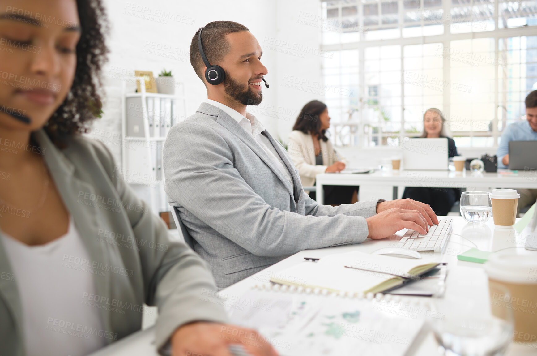Buy stock photo Young cheerful mixed race male call center agent answering calls while wearing a headset at work. Hispanic businessman talking on a call while typing on a desktop computer at a desk in an office