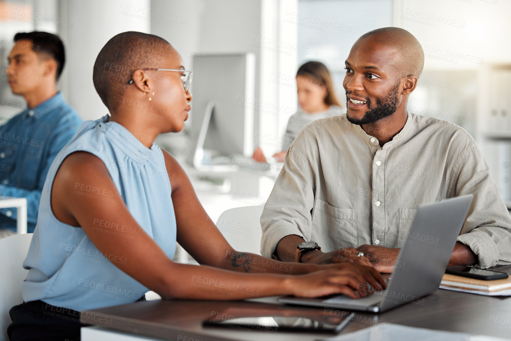 Buy stock photo Two businesspeople having a meeting together in an office at work. Young african american businesswoman talking to a colleague while typing on a laptop. Coworkers planning and using a laptop at work