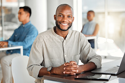 Buy stock photo Portrait of a young cheerful african american businessman working on a laptop in an office. One happy and positive male businessperson smiling while working in an office