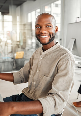 Buy stock photo Portrait of a young cheerful african american businessman sitting at a desk alone at work. One joyful and positive male businessperson smiling while working in an office
