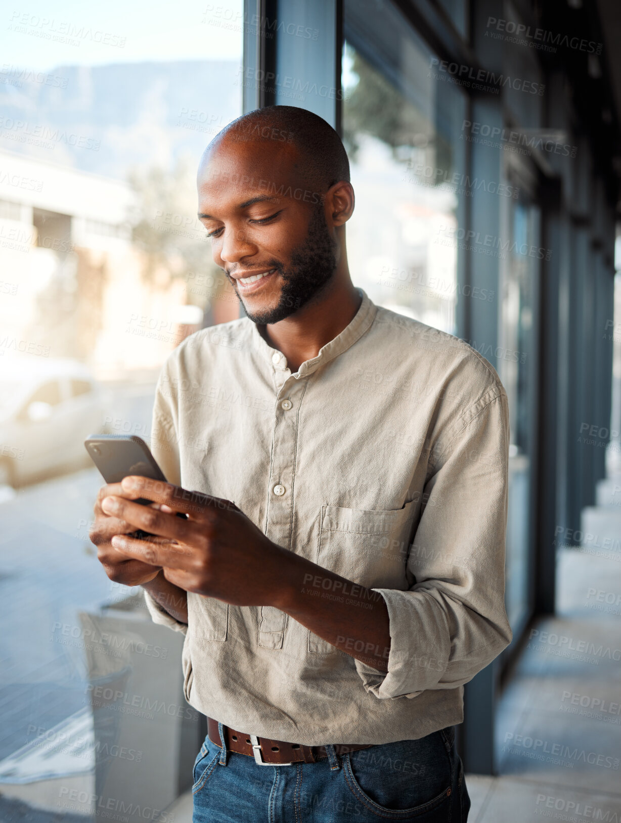 Buy stock photo Young african american businessman typing a message on a phone at work. Happy male business professional using social media on a cellphone while standing in an office on a break at work