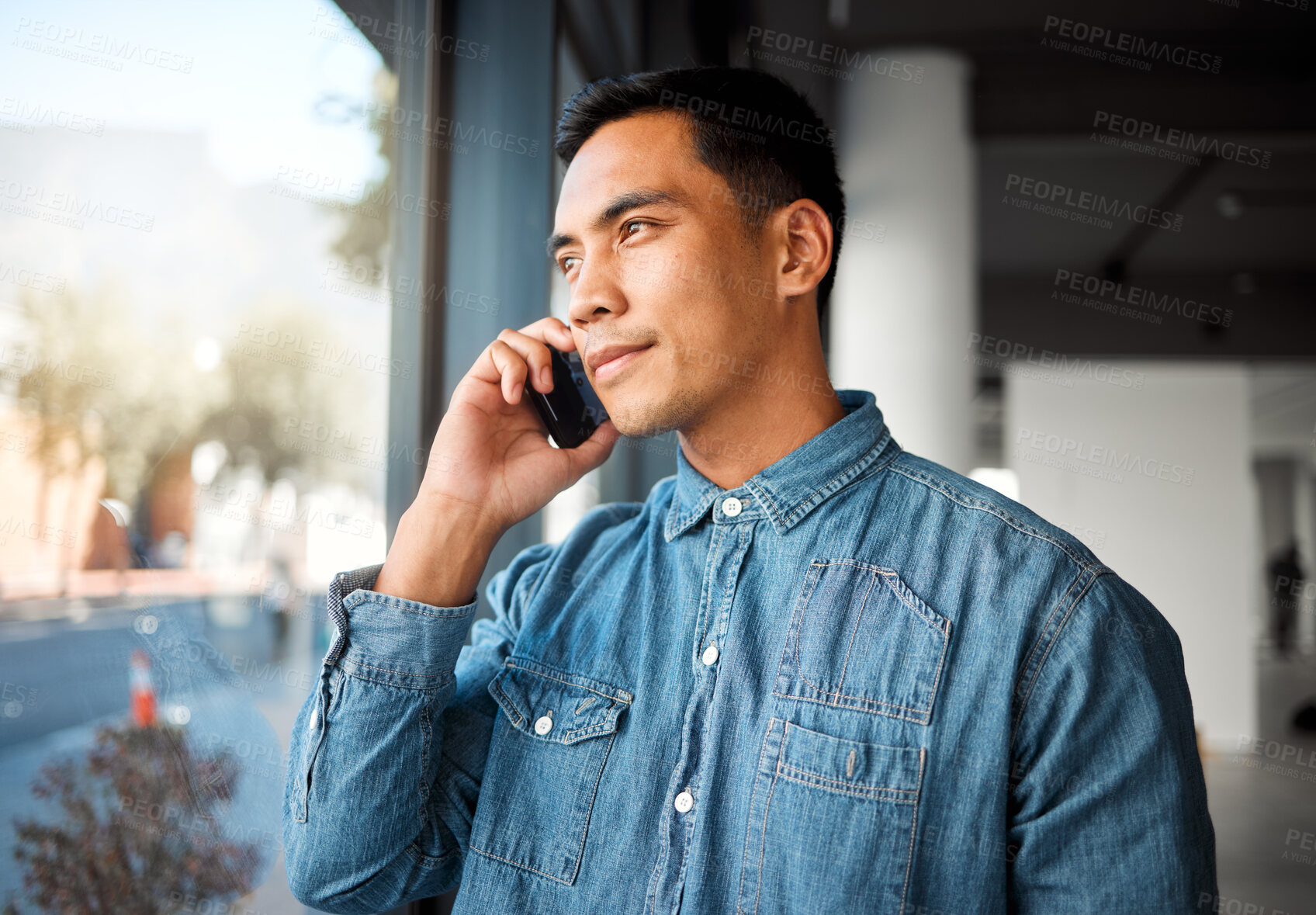Buy stock photo Young asian businessman on a call using a phone at work. Content chinese male business professional talking on a cellphone while standing in an office on a break at work