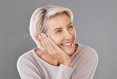 One happy caucasian mature woman isolated against a grey studio background, posing with a hand on her cheek and thinking about making a decision. Ageing woman touching her face while smiling