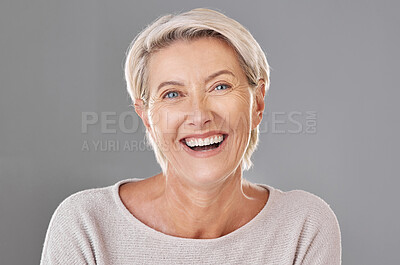 Portrait of one happy caucasian mature woman isolated against a grey sopyspace background. Confident smiling senior woman looking cheerful while showing her natural looking teeth in a studio