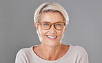Portrait of one beautiful caucasian mature woman isolated against a grey studio background wearing glasses. Senior woman smiling and showing her bright dentures in a studio