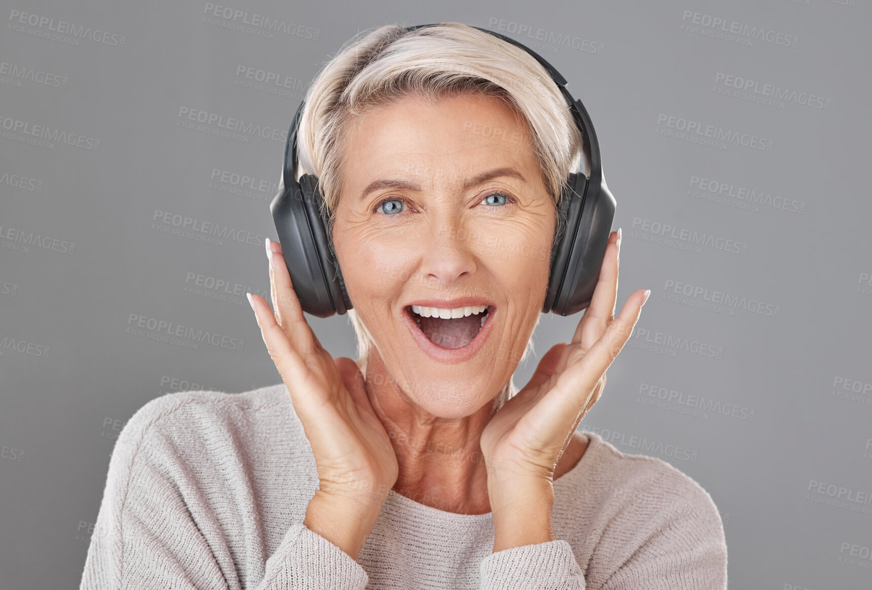 Buy stock photo One happy mature woman isolated against a grey background in a studio and wearing headphones to listen to music. Smiling caucasian senior enjoying the loud music and looking youthful and playful