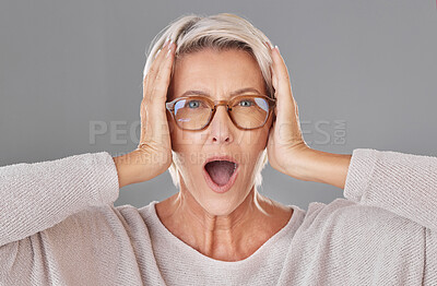 Portrait of one beautiful caucasian mature woman isolated against a grey studio background and expressing shock while wearing glasses. Senior woman making facial expressions and looking surprised