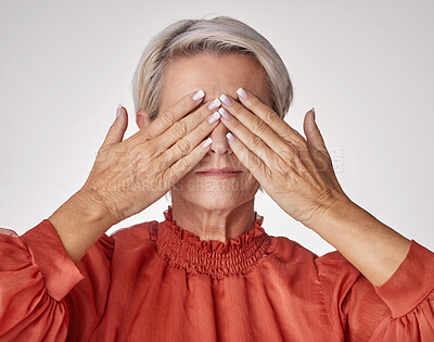 Buy stock photo Senior, hands and covering eyes or face of mature woman suffering with a headache or eye strain while posing against a grey studio background. Elderly woman having problems with her vision or sight.