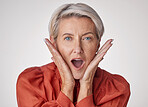 Portrait of one beautiful caucasian mature woman isolated against a grey studio background and expressing  shock. Senior woman making facial expressions and looking surprised