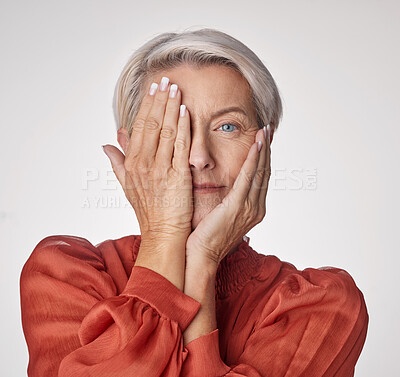 Portrait of one beautiful caucasian mature woman isolated against a grey studio background and playfully holding her hands over her face. Ageing woman testing her eyesight