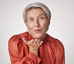 One happy mature caucasian woman blowing a kiss with her hands against a grey background. Ageing female using body language to express love, kindness, flirting and affection with a gesture