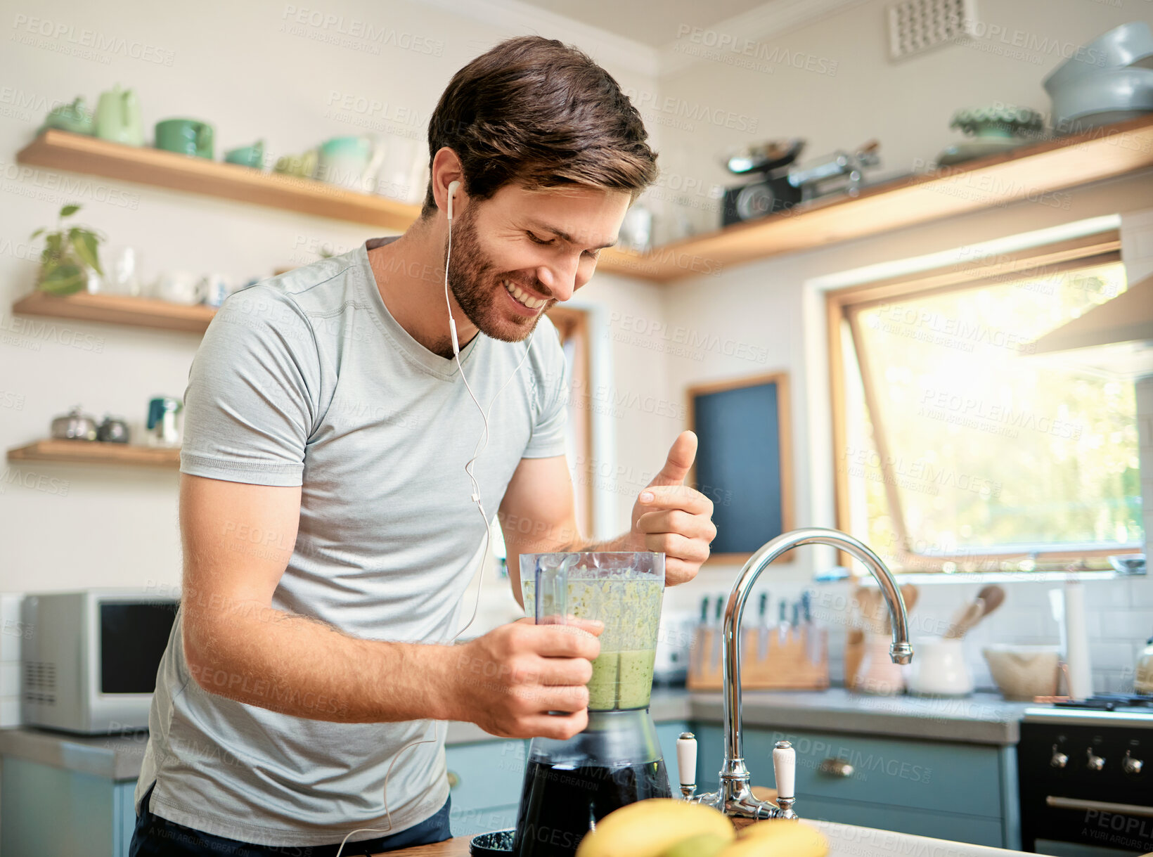 Buy stock photo One fit young caucasian man using blender to make healthy green detox smoothie while wearing earphones in kitchen at home. Guy having fresh fruit juice to cleanse and provide energy for training. Wholesome drink with vitamins and nutrients