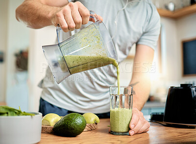 Closeup of one caucasian man pouring healthy green detox smoothie from blender into glass in kitchen at home. Guy having fresh fruit juice to cleanse and provide energy for training. Wholesome drink with vitamins and nutrients