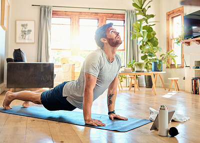 Buy stock photo One fit young caucasian man doing cobra push up bodyweight exercise while training with online tutorial on digital tablet at home. Focused guy challenging himself to gain muscle, core strength and increase endurance during yoga workout
