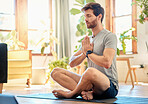 One young caucasian man sitting with legs crossed and eyes closed meditating in harmony with hands together in namaste gesture while practising yoga at home. Calm, relaxed and focused guy feeling zen while praying quietly for stress relief and peace