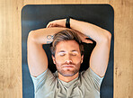 One fit young man from above relaxing with eyes closed in meditation while lying on a yoga mat and taking a break from exercise at home. Face of tired guy taking a nap or sleep to rest after workout on wooden floor