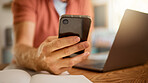 Man using a phone while working from home alone. One businessperson working on a laptop and writing in a notebook while using social media on a cellphone and sitting at a table in the morning at home