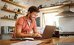 Young cheerful caucasian businessman working on a laptop at home alone. Happy male businessperson smiling and typing an email on a computer while working in the kitchen at home