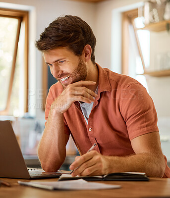 Cheerful young caucasian businessman writing in a notebook and working on a laptop at home alone. Happy male businessperson smiling and taking notes in a diary while working in the kitchen at home