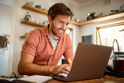Cheerful caucasian businessman working on a laptop at home alone. Happy male businessperson smiling and typing an email on a computer while working in the kitchen at home