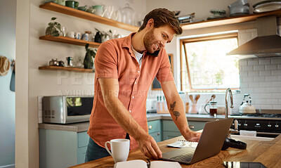 Young content caucasian businessman on a call using a cellphone while working on a laptop and drinking coffee at home alone. Happy male businessperson smiling and talking on a cellphone while working in the kitchen at home