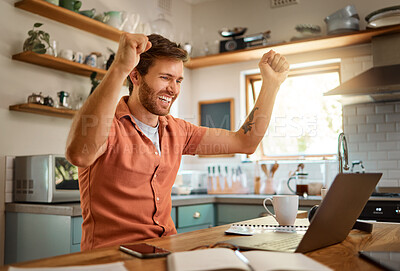 Young cheerful caucasian businessman cheering with joy while working on a laptop at home alone. One joyful male businessperson smiling while working in the kitchen at home
