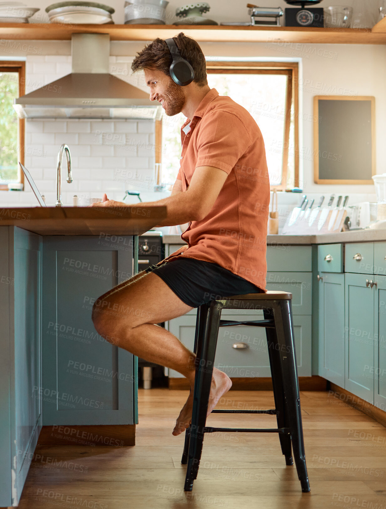 Buy stock photo Laptop, headphones and remote work, happy man at kitchen counter for email, social media or networking. Technology, online job and smile, freelancer on internet for music, podcast or research article