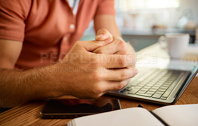 Man using a laptop and notebook while working from home alone. Businessperson working on a laptop and writing in a notebook sitting at a table in the morning at home