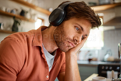 Young tired caucasian businessman wearing headphones and listening to music while working from home alone. One stressed businessman looking unhappy while working at home. Person looking upset and worried