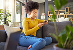 Young mixed race woman typing a message on a phone at home. One hispanic female with a curly afro using social media on a cellphone while relaxing on the couch at home