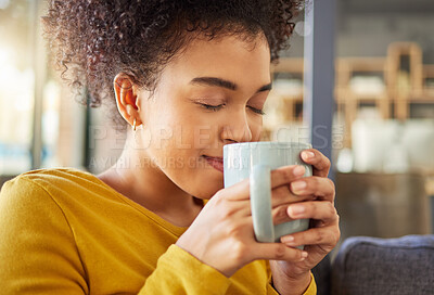 Young happy mixed race woman holding and drinking a cup of coffee at home. One cozy hispanic female smelling and enjoying a cup of tea while relaxing at home